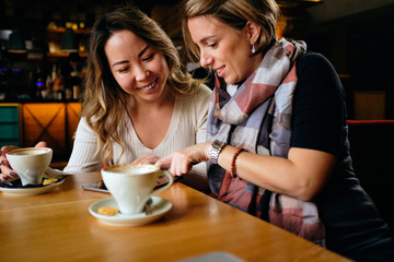 Two female friends in a cafe having coffee, smiling and chatting	