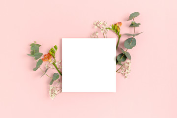 Blank paper card mockup with frame made of flowers and eucalyptus. Floral composition with copy space on a pink pastel background.