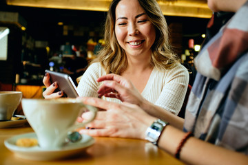 Two female friends in a cafe having coffee, smiling and chatting	