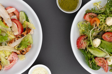 white deep plates with fresh salad ingredients mixed with sauce placed on an gray background. A place for a menu, banner or advertisement