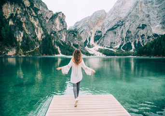 Romantic girl with long hair loose, turned away, walk spread hands on wooden pier Lake Braies....