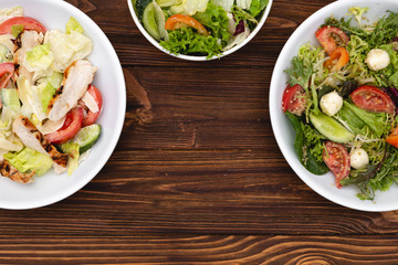 white deep plates with fresh salad ingredients mixed with sauce placed on a rustic background. A place for a menu, banner or advertisement