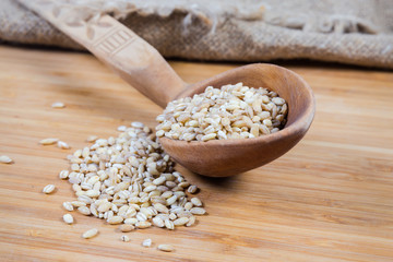 Raw pearl barley in wooden spoon on wooden surface closeup