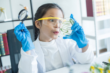 little asian girl elementary school looking into magnifying glass at the aloe vera in tray on desk at school. scientist making experiments in home laboratory. child and science. education concept.