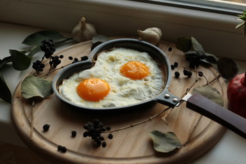 Close up of fried eggs in a heart shaped pan with ingredients around