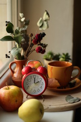 Two o'clock in the afternoon on a clock in retro style on a windowsill, around apples, flowers and a cup and saucer