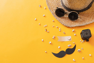 Summer traveling to the sea with straw hat, sun glasses, camera,paper mustache, shells on yellow...