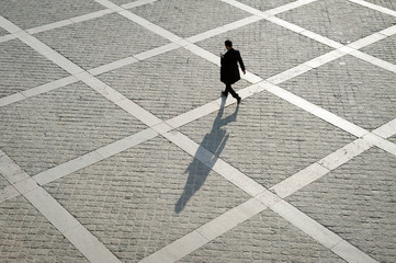 Overhead view of unrecognizable pedestrian casting shadow on the geometric patterns of a stone plaza on a quay next to the River Seine in Paris, France