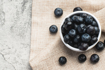 Fresh heap of blueberry in white clean bowl on sack cloth on minimal clean cement background. Healthy food, Fresh fruit, Vitamin and fiber source concept.