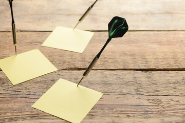 Darts with paper sheets on wooden background