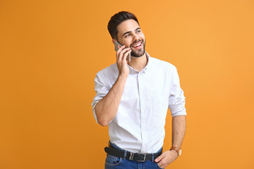Handsome young man talking by phone on color background
