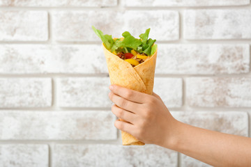 Female hand with tasty doner kebab on brick background
