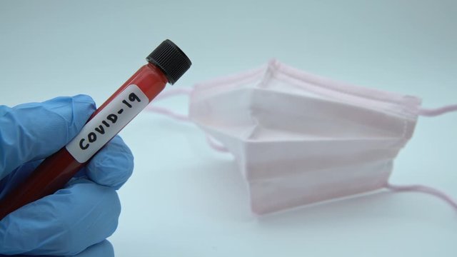 4K, Face mask and test tube with infected blood sample for COVID-19, novel coronavirus found in Wuhan, China. Scientist with blue gloves for protection. Vaccine research for the virus 2019-nCoV-Dan