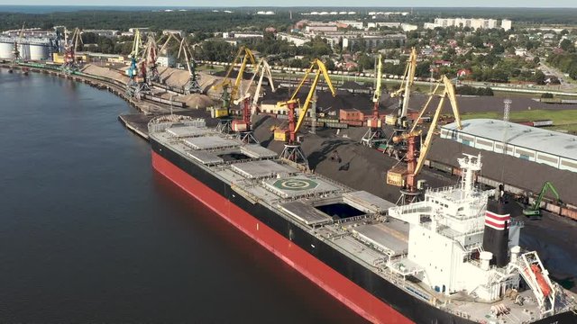 VENTSPILS, LATVIA - JULY, 2019: Aerial view of big dry cargo ship and port cranes that loads cargo in port of Ventspils.