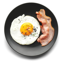 Plate with fried egg and bacon on white background