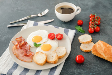 Plate with fried eggs, bacon and bread on dark background