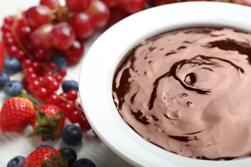 Bowl with tasty chocolate fondue and berries on white table, closeup