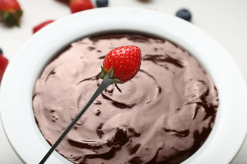 Bowl with tasty chocolate fondue and strawberry on table, closeup