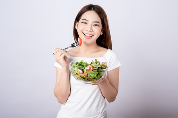 Beautiful young asian eating salad with big smile happy beaming face in seamless white  isolated...