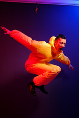 An Asian man in a yellow chemical protection suit screams in a jump on a colored trend background.