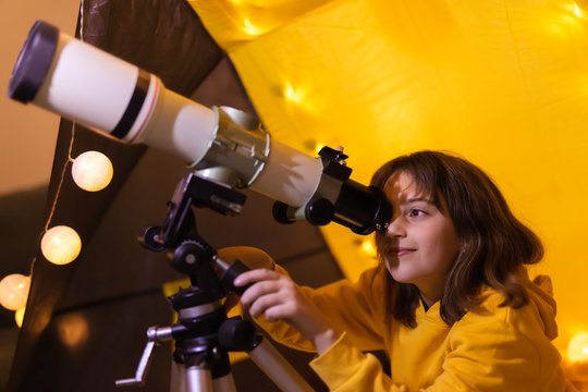 Small girl using telescope at home living room in a tent.