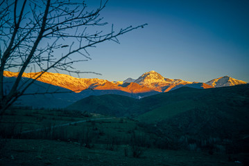a sunset view of mountains covered with snow in the fall season in  the north of Iraq Kurdistan Region with green landscape and trees in the foreground