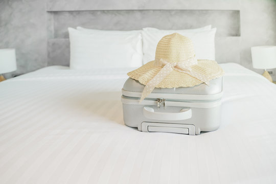 hat and grey luggage on white bed in bedroom of hotel