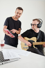 Writer showing tablet computer with new song lyrics to composer who is sitting at workplace with...