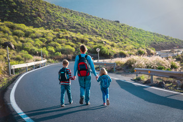 father with two kids walking on road, travel in mountains