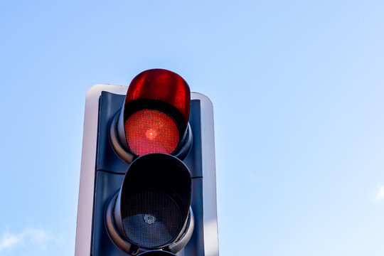 British traffic light/signal illuminated red to indicate to traffic to stop, set against a blue sky on a sunny day.