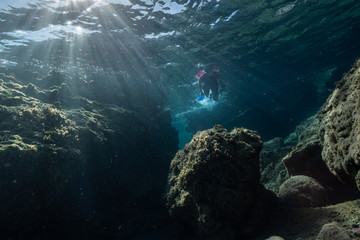 Woman freediver glides with fins. over rocky bottom sea. Freediving and beautiful light in blue sea.