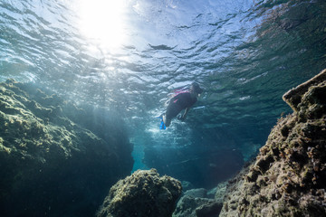 Woman freediver glides with fins. over rocky bottom sea. Freediving and beautiful light in blue sea.