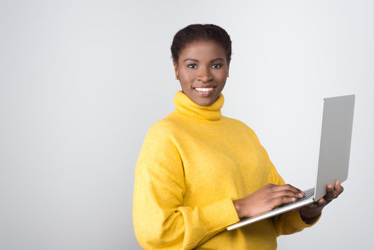 Beautiful smiling African American woman using laptop. Attractive young lady with modern device looking at camera. Technology concept
