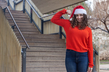 Portrait of rich attractive caucasian young woman with Santa Claus's hat taking a lot of money dollars, in the park, orange sweater and jeans, long curly hair. Place for your text in copy space.