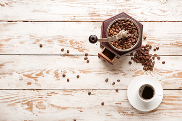 Coffee-grinder and cup of hot beverage on wooden background