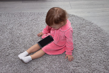 Fototapeta premium beautiful little girl with a smartphone on the carpet in her room.