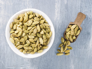 Spice green cardamom (Elettaria cardamomum) in a ceramic white bowl with wooden scoop on gray concrete background. The proper nutrition concept