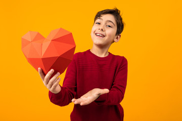smiling handsome caucasian boy with paper heart for valentines day on orange background
