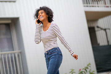 smiling african american woman walking and talking with phone outside