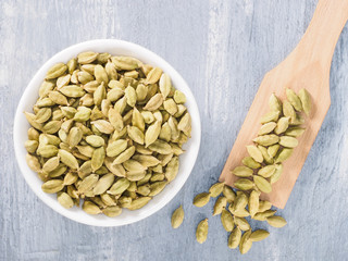 Spice green cardamom (Elettaria cardamomum) in white ceramic bowl and wooden spatula on gray concrete background closeup. The proper nutrition concept