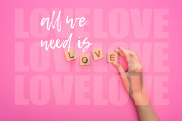 partial view of woman holding cubes with all we need is love lettering on pink background