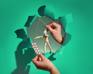 Dependence on pharmaceuticals concept. Sinister hands controlling puppet with face mask and hold...