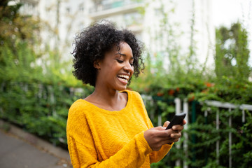 Fototapeta na wymiar happy young black woman looking at mobile phone outdoors