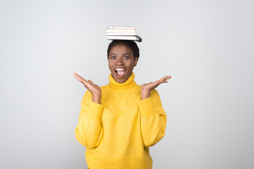 Amazed beautiful African American woman with books on head. Agitated young lady looking at camera....