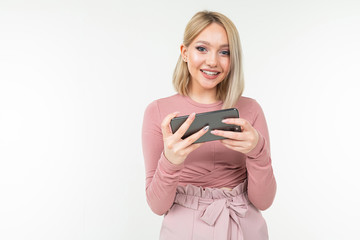 Fototapeta premium Caucasian blond girl in pink clothes plays on the phone in horizontal format on a white background