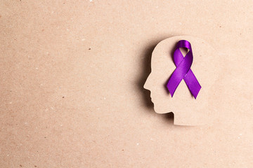 Purple awareness ribbon and head silhouette on a brown cardboard background. E