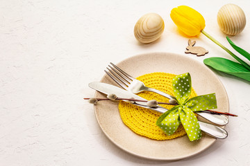 Easter table setting on textured white putty background. Spring holiday card template. Cutlery, knitted napkin, egg, bunny, tulip