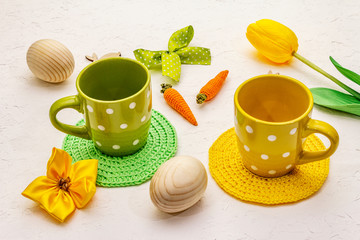 Easter table setting on textured white putty background. Spring holiday card template. Cutlery, knitted napkin, egg, bunny, tulip, polka dot cup