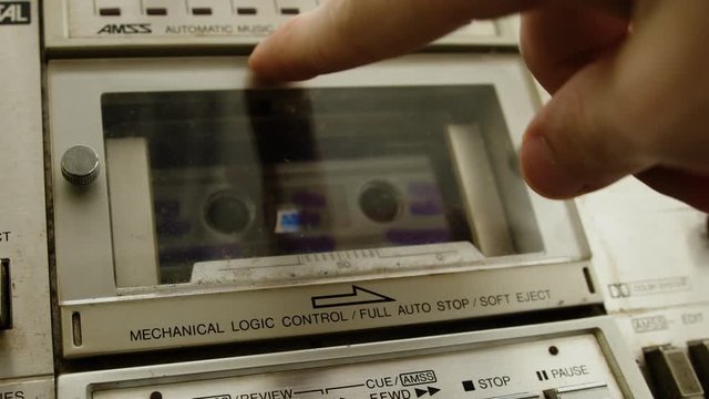 The old cassette player inserts a cassette into the boombox and presses the play button. Retro cassette player concept.