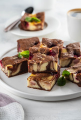 Cheesecake brownies with raspberry stacked on a white plate.